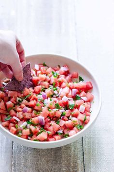 a person dipping a tortilla chip into a bowl of watermelon salsa