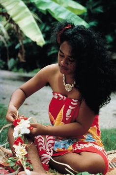 a woman is sitting on the ground with flowers in her hand and smiling at something