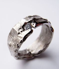 a close up of a silver ring on a white surface with a diamond in the middle