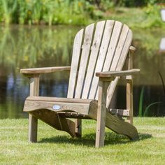 a wooden chair sitting on top of a lush green field next to a lake in the background