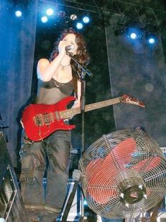 a woman singing into a microphone while holding a guitar in front of an air conditioner