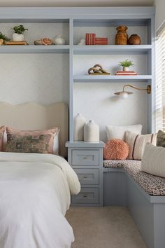 a white bed sitting under a window next to a shelf filled with lots of books