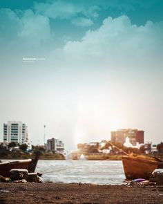 two boats on the beach with buildings in the background and blue sky above them,