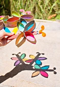 someone is holding up some paper flowers on the ground with their shadow in the background