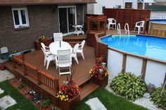 an above ground pool surrounded by wooden decking and white lawn chairs with flowers on them