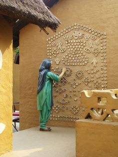 a woman standing next to a wall covered in lots of small carvings and decorations on it's side