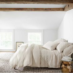 a bed with white linens in a bedroom next to two windows and a rug on the floor