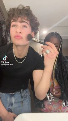 a young man is brushing his teeth in front of a mirror while another woman looks on