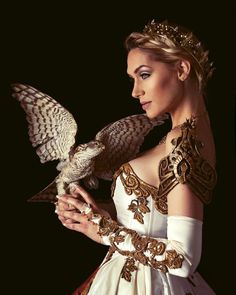 a woman in a white and gold dress holding an owl on her arm with wings outstretched