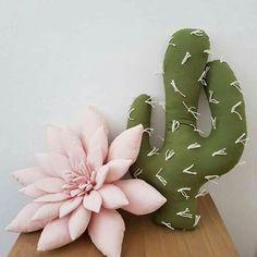 a pink flower sitting on top of a wooden table next to a green cactus plant