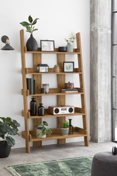 a wooden shelf with plants and pictures on it in front of a window, next to a couch