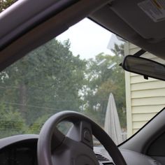 the interior of a car with trees in the back ground and houses in the background