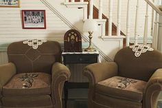 two brown chairs sitting next to each other in front of a stair case with pictures on the wall