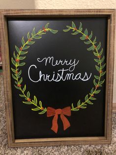 a chalkboard with the words merry christmas written on it and a wreath in front