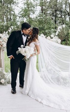 a bride and groom kissing in front of an arch with white flowers on the side