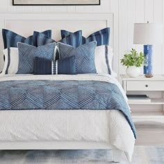 a bed with blue and white pillows on top of it next to a night stand