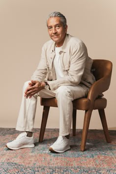 an older man sitting in a chair with his hands on his knees and looking at the camera