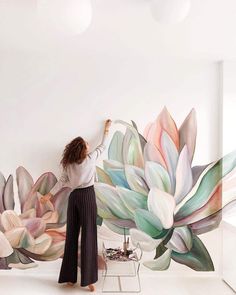 a woman standing in front of a wall with flowers painted on it and painting the walls