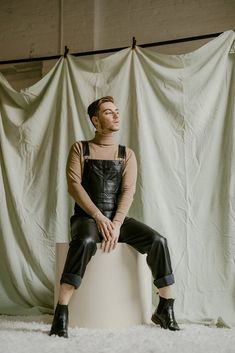 a man sitting on top of a white stool in front of a curtained wall