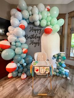 a birthday party with balloons and decorations in the shape of an arch, including a baby's high chair