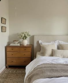 a bed with white linens and pillows in a bedroom next to a wooden dresser