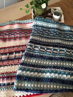 two crocheted blankets sitting on top of a table next to a potted plant