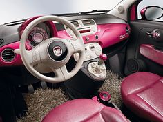 the interior of a small car with pink leather seats and steering wheel covers on display