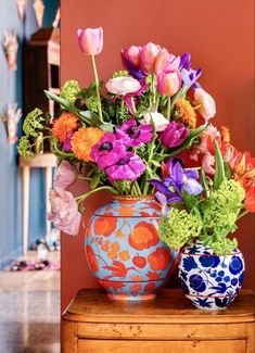 two vases filled with colorful flowers sitting on top of a wooden dresser next to a wall