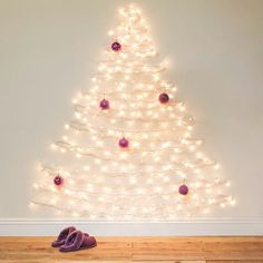 a white christmas tree with lights and slippers on the floor in front of it