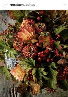 a vase filled with lots of flowers on top of a wooden table covered in leaves and berries