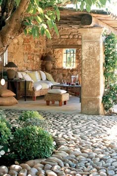 an outdoor living area with stone flooring and furniture under a tree in the shade