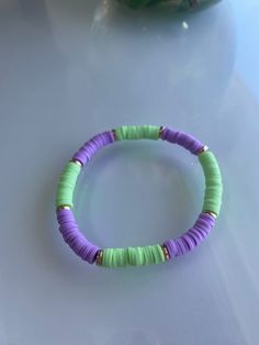 a purple and green beaded bracelet sitting on top of a white table next to a vase