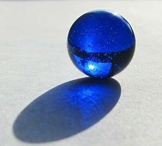 a blue glass ball sitting on top of a white surface with a shadow from it