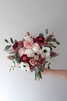 a person holding a bouquet of flowers in their hand with white and pink blooms on it