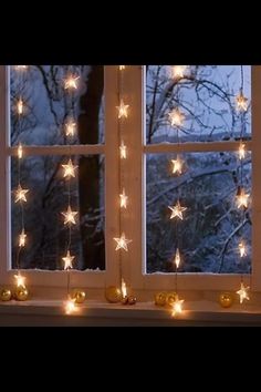 an open window with christmas lights hanging from the windowsill and snow covered trees in the background