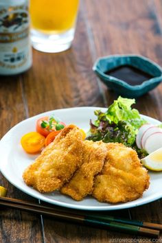 fried chicken and vegetables on a white plate with chopsticks next to the plate