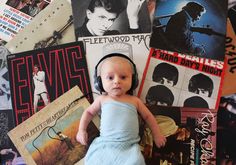 a baby with headphones on laying in front of many records and posters, all looking at the camera