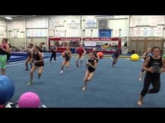 a group of people are running around in a gym with balloons and balls on the floor