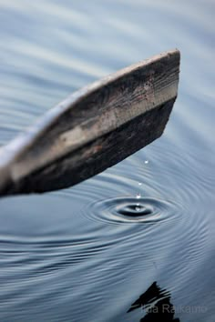 a small wooden boat floating on top of a lake next to a shore line with ripples in the water