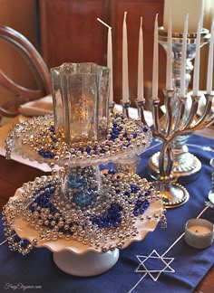 a table topped with candles and dishes filled with blue beaded decorations on top of each other