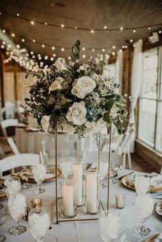 a centerpiece with candles and flowers on a white table cloth at a wedding reception