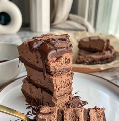 a piece of chocolate cake on a white plate with a fork and cup in the background