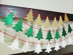 paper christmas trees are hanging from a string on a mantle in front of a wood paneled wall