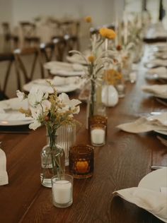 the table is set with white and yellow flowers in glass vases, candles, and napkins