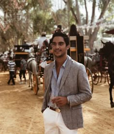 a man standing in front of horses and buggies on a dirt road with a drink in his hand