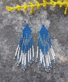 two pairs of blue and white beaded earrings on top of a gray surface with yellow flowers in the background