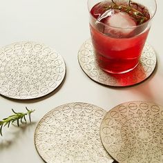 three coasters with different designs on them and a drink in the middle one has a sprig of rosemary