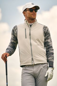 a man holding a golf club while wearing sunglasses and a white jacket with camouflage print on it