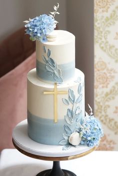 a three tiered cake with blue flowers and a cross on top