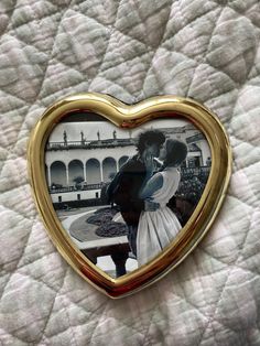 a gold heart shaped photo frame with a couple kissing in it on top of a bed